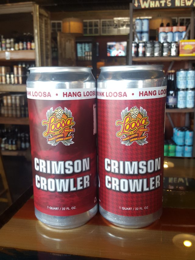 Two Crimson Crowler cans on the bar top, bottle shelves glowing behind them