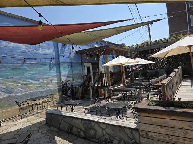 The Hang Loosa patio in daylight — shade sails stretched overhead, umbrellas, wrought-iron tables and the beach mural along the wall