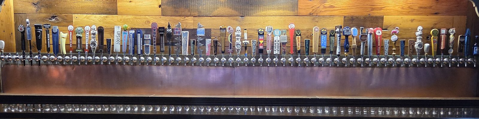 The full run of Loosa Brews tap handles above the copper bar rail — sixty-three lines side by side on reclaimed wood